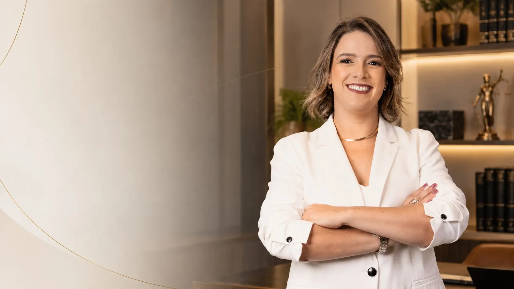Dra. Luciana Frutuoso de Abreu, de blazer branco e braços cruzados, em seu escritório